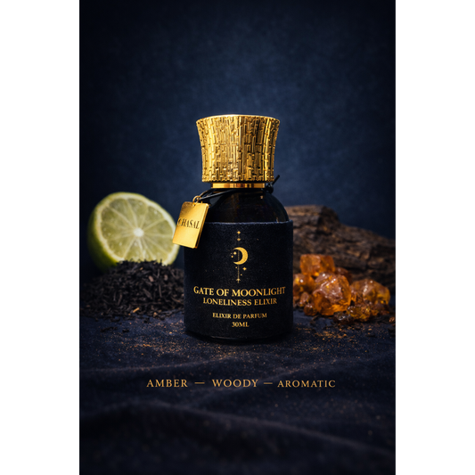 Schwarzer Flakon des Loneliness Elixiers mit goldener Kappe, umgeben von einer Limette, schwarzem Tee und Harzstücken – Mystischer Nischenduft von CHASAL